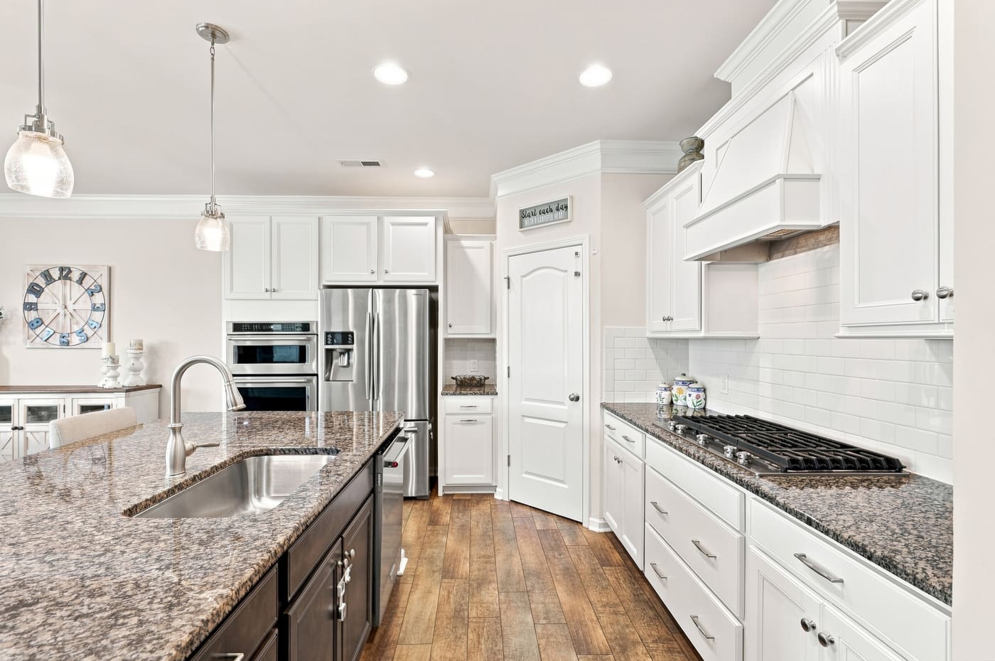 The gas cooktop under a hood, with tile backsplash and granite counters running to the pantry door.